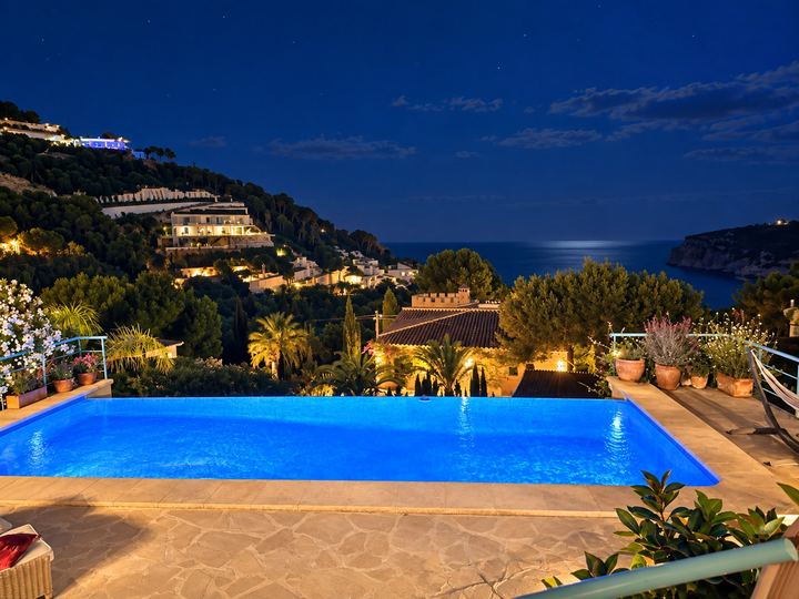 La piscina iluminada de noche, con el mar al fondo